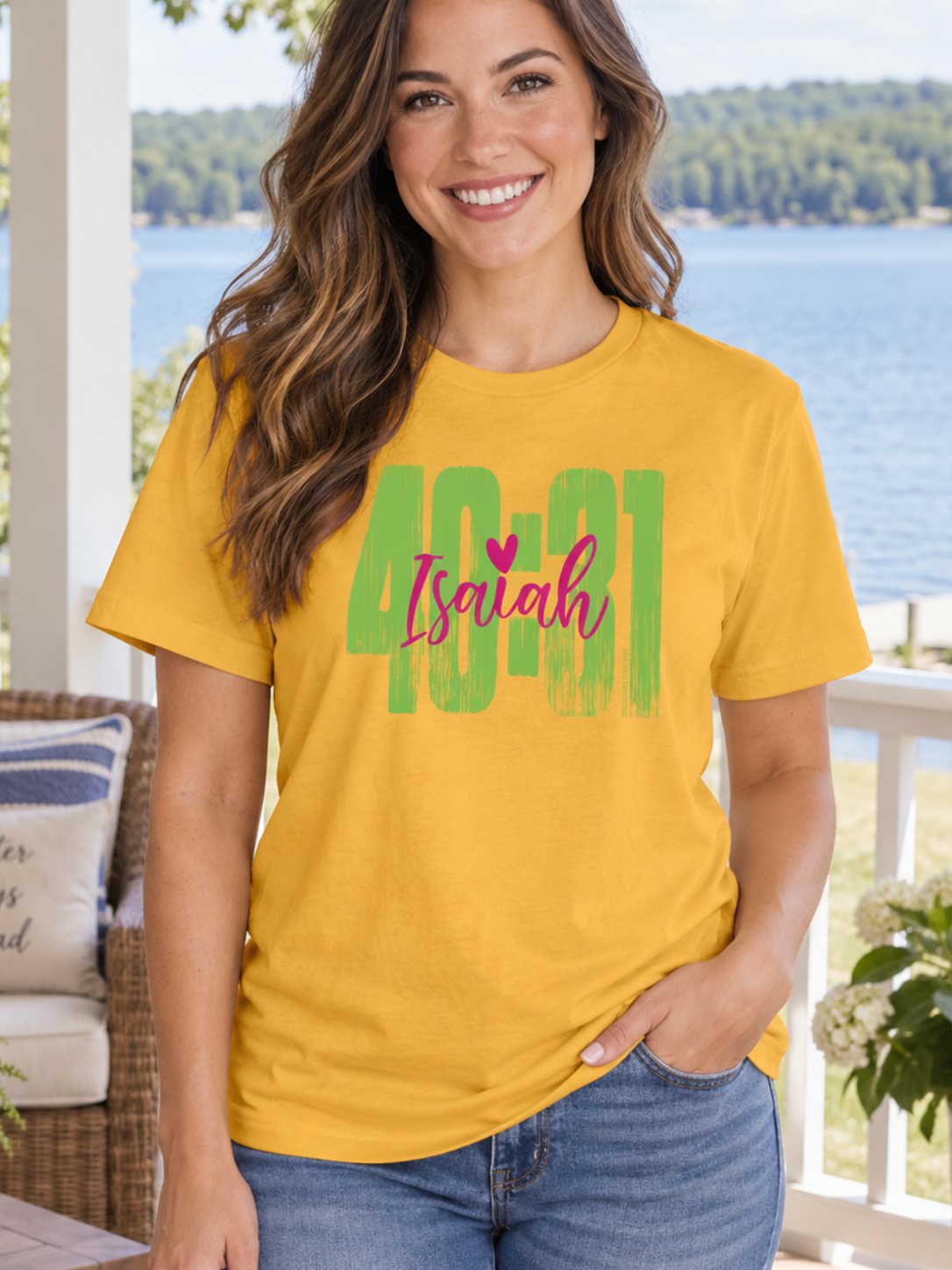 A woman stands on a porch by a lake wearing a bright yellow graphic T-shirt with the text '40:41' and 'Isaiah' in pink and green, paired with blue jeans.