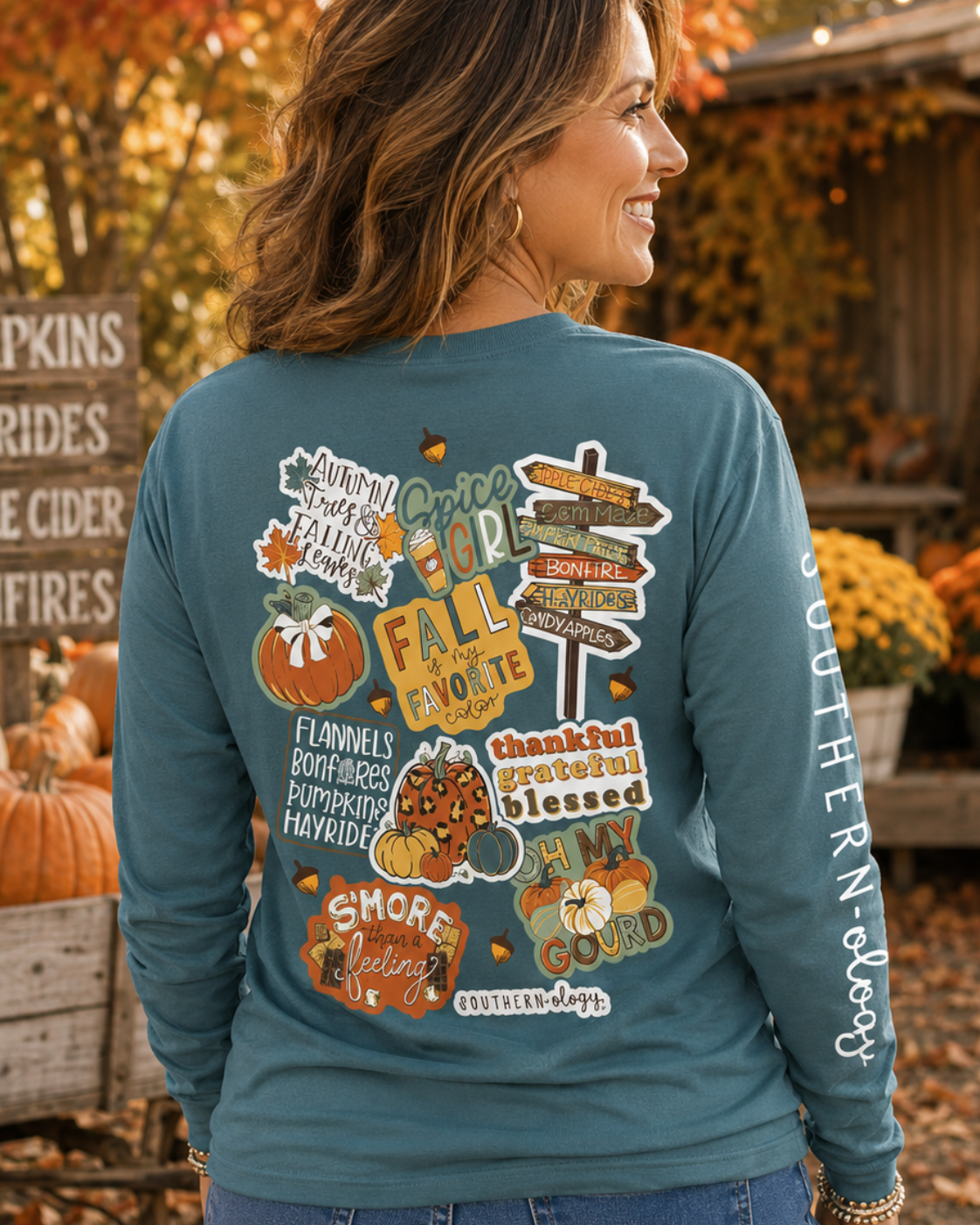 Woman wearing a teal long-sleeve shirt with fall-themed designs in an autumn setting.